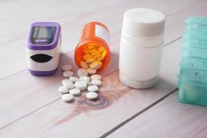 Pulse oximeter, medical pills and container on table photo