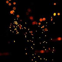 Particles of burning embers fly and glow isolated in the night sky. Bright yellow sparks on a black background, yellow bright round bokeh. photo