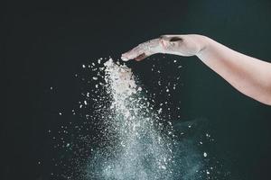 Isolated on black background female hand pours white flour like snow for baking photo