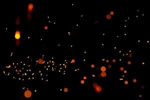 Particles of burning embers fly and glow isolated in the night sky. Bright yellow sparks on a black background, yellow bright round bokeh. photo