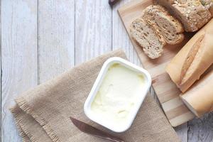 Mantequilla en recipiente y pan integral en la mesa foto