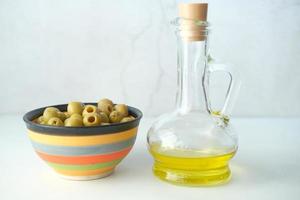 Bottle of olive oil and fresh olive in a container on table photo