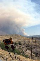 Billowing smoke from current Gila National Forest Johnson fire behind curved road sign in old burn photo