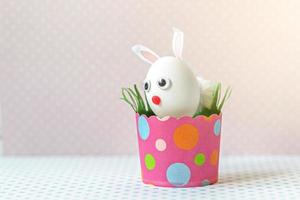 White chicken egg with bunny ears and a muzzle in an environmentally friendly pink paper tray photo