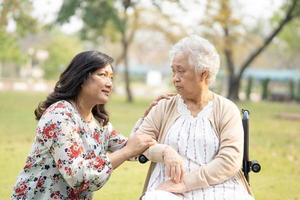 Paciente asiático mayor o mayor de la mujer de la señora mayor con cuidado, ayuda y apoyo en silla de ruedas en el parque en concepto médico fuerte sano de las vacaciones.