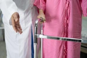 El médico ayuda y cuida a la anciana asiática mayor o anciana que usa un andador con una salud fuerte mientras camina en el hospital.