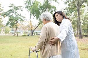 médico ayuda y cuidado anciana asiática anciana o anciana usa andador con una salud fuerte mientras camina en el parque en felices vacaciones frescas. foto