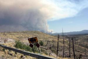 Billowing smoke from current Gila National Forest Johnson fire behind curved road sign in old burn photo