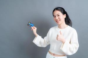 Portrait of a lovely young Asian woman in sweater showing credit card with copy space photo