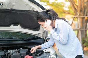 Mujer joven de pie cerca del coche averiado con el capó levantado que tiene problemas con su vehículo foto