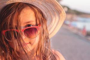 Portrait of a beautiful little girl with sunglasses and straw hat on the beach, with copy space