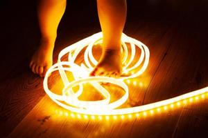 Baby legs, little girl stepping on LED strip, naughty baby playing with electricity, child safety concept and parental control  close-up photo