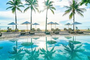 Beautiful luxury umbrella and chair around outdoor swimming pool in hotel and resort with coconut palm tree on sunset  or sunrise sky photo