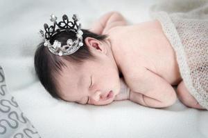 Newborn baby girl sleeping and wearing a silver crown. photo