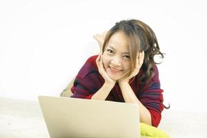 Asian woman smiling and lying on carpet with laptop at home. Work from home concept. photo