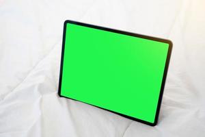 Top view of black tablet on a bed with green chroma key. photo