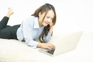 Asian woman working with laptop while lying on carpet at home. Work from home concept. photo