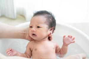 El recién nacido está siendo bañado por su madre usando una tina en casa.