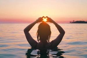 Back view of asian woman making heart sign in the sea. Vacation vitality healthy living concept. Silhouette hand in heart shape. photo