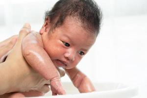 El recién nacido está siendo bañado por su madre usando una tina en casa.