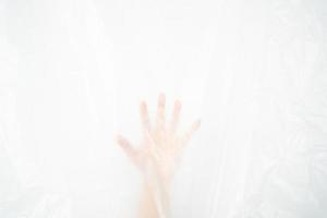 Blurred hand pushing behind the plastic sheet on white background. Stop using the plastic concept. photo