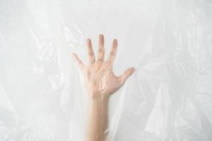 Hand pushing behind the plastic sheet on white background. Stop using the plastic concept. photo