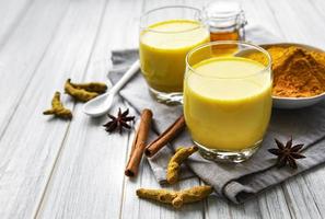 Yellow turmeric latte drink. Golden milk with cinnamon, turmeric, ginger  and honey over white marble background. photo