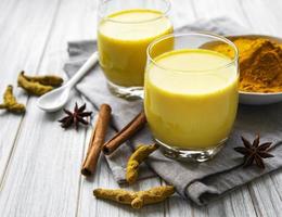Yellow turmeric latte drink. Golden milk with cinnamon, turmeric, ginger and honey over white marble background photo