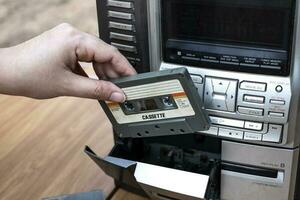 Mano de mujer poniendo cassette en el antiguo reproductor de cintas de audio sobre fondo de madera de escritorio superior foto