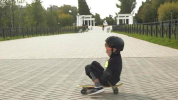un niño en edad preescolar con un casco protector monta una patineta en el parque de verano