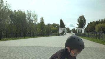 Ein Vorschuljunge mit Schutzhelm fährt im Parksommer auf einem Skateboard