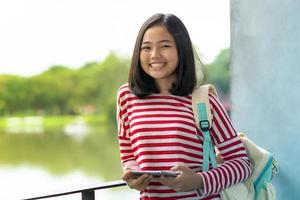Chica estudiante asiática con una tableta digital en el parque en un día soleado de verano