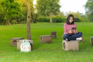 Chica estudiante asiática usando una tableta digital en el parque escolar en un día soleado de verano