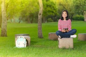 Chica estudiante asiática usando una tableta digital en el parque escolar en un día soleado de verano