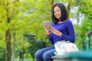 Chica estudiante asiática usando una tableta digital en el parque en un día soleado de verano foto