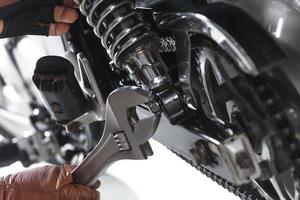 Cropped view of Mechanic using a wrench on a motorcycle on white background photo