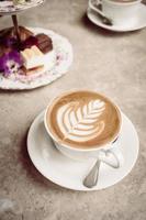 taza blanca con café con leche y pastel