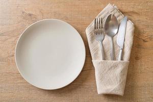 Empty plate or dish with knife, fork, and spoon on wood tile background photo