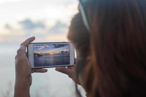 persona que toma un video de la puesta de sol con un teléfono inteligente foto