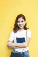 Retrato de hermosa estudiante universitaria está sonriendo sobre fondo de pared amarilla