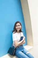 Retrato de hermosa estudiante universitaria está sonriendo sobre fondo de pared azul foto