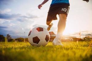 deportes de acción al aire libre de un grupo de niños que se divierten jugando fútbol soccer para hacer ejercicio en una zona rural comunitaria bajo el crepúsculo del atardecer. foto