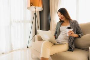 Beautiful young asian portrait using computer and laptop with coffee cup sitting on sofa photo