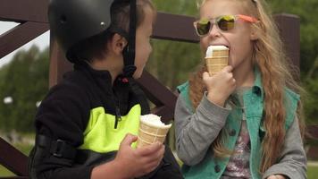 un ragazzo e una ragazza sono seduti su una panchina del parco e mangiano un gelato d'estate video