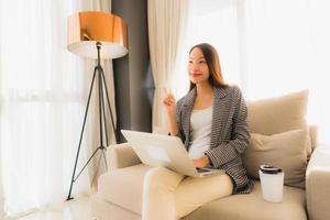 Beautiful young asian portrait using computer and laptop with coffee cup sitting on sofa photo