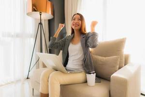 Beautiful young asian portrait using computer and laptop with coffee cup sitting on sofa photo