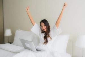 Retrato de hermosas mujeres asiáticas jóvenes con taza de café y computadora portátil en la cama foto