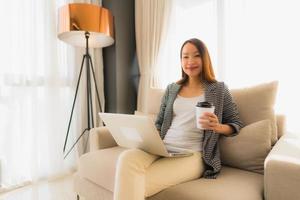 Beautiful young asian portrait using computer and laptop with coffee cup sitting on sofa photo