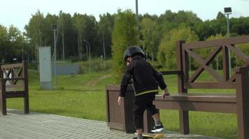 un niño en edad preescolar con un casco protector monta una patineta en el parque de verano