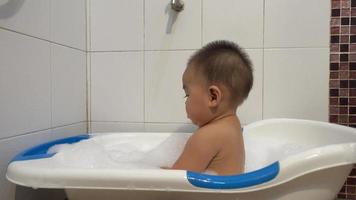 feliz bebê asiático garotinho tomando banho brincando com bolhas de espuma, pia água, criança engraçada tomar banho com espuma de sabão no banheiro interior em casa, cuidados de saúde e higiene